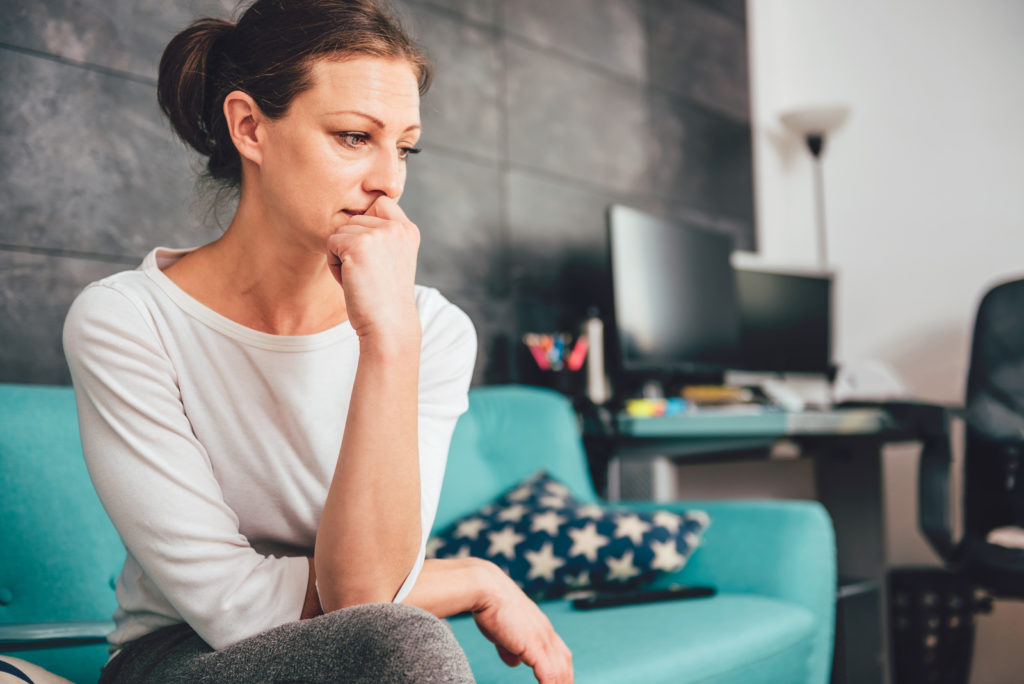 A distressed looking woman sitting on a couch thinking